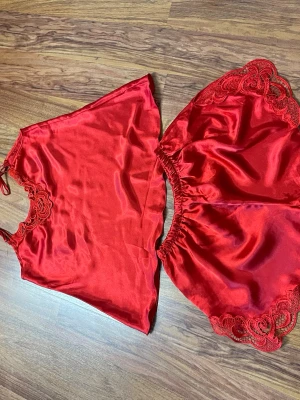 Rött satinsovset med spetsdetaljer - Snyggt rött sovset i satin med linne och shorts. Linnet har tunna axelband och spetsdetaljer vid ringningen. Shortsen har elastisk midja och matchande spets längs bensluten. Perfekt för dig som gillar mjuka material och en lyxig känsla.