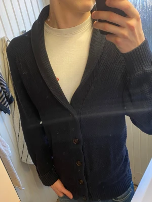 Mörkblå kofta från John Lewis - Snygg mörkblå kofta från John Lewis med sjalkrage och träknappar framtill. Koftan är stickad i ett tjockare material och har ribbade muddar vid ärmslut och nederkant. Perfekt att slänga över en t-shirt för en avslappnad look.