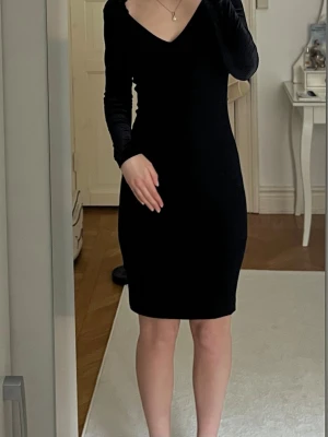 Svart klänning - Snygg svart klänning med v-ringad hals och långa sammet ärmar. Klänningen har en kroppsnära passform och slutar ovanför knäna.