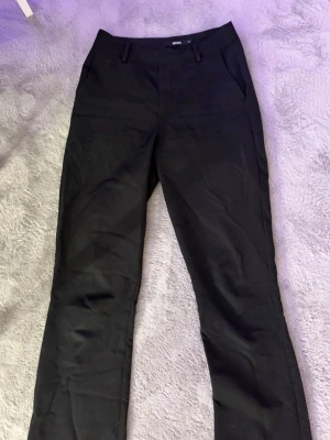 Svarta kostymbyxor från Bik Bok - Snygga svarta kostymbyxor från Bik Bok med raka ben, lite utsvängning och klassiska bälteshällor. Byxorna har diskreta sidofickor och är perfekta för en clean och stilren look. Materialet känns mjukt och följsamt, vilket gör dem bekväma att bära hela dagen.