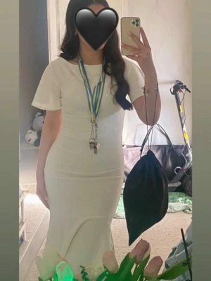 Studentklänning - Vit långklänning med volang - Säljer en elegant vit långklänning med korta ärmar och volang nertill. Klänningen har en figurnära passform och rund halsringning. Perfekt för student eller sommarens speciella tillfällen. Materialet känns mjukt och lätt, troligen bomull eller polyester.