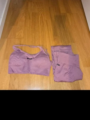 Lila seamless träningsset från Bootee - Säljer ett seamless träningsset från Bootee i lila färg från Seriern Supersculpt. Setet består av en sport-bh med smala axelband och matchande tights med hög midja och scrunch. Materialet är stretchigt och följsamt, perfekt för träning och rörelse. Diskret Bootee-logga på både bh och tights.