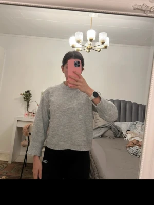 Ljusgrå stickad tröja - Mysig ljusgrå stickad tröja med rund halsringning och ribbade muddar vid ärmslut och nederkant. Tröjan har en rak passform och är perfekt för lager på lager. Passar till både jeans och mjukisbyxor. Materialet känns mjukt och bekvämt.