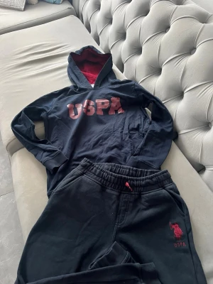 Marinblå mjukiset från US polo - Snygg marinblå hoodie och mjukisbyxor från US polo med röd insida i huvan och stora röda bokstäver på bröstet. Notera att hoodien är i storlek 12-13 år eller 152 till 158 cm medans byxorna är i storlek 11-12 år eller 146-152 cm. Hör av dig om du endast vill köpa en av varorna, pris går att diskutera!