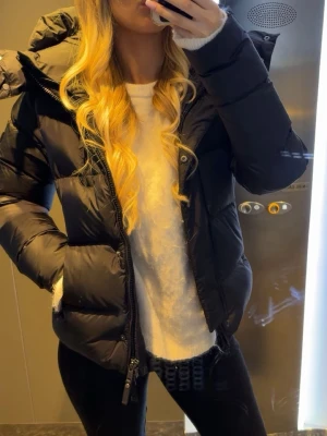 Svart cedrico jacka - Intressekoll!! Snygg svart cedrico jacka med stor huva och dragkedja framtill. Jackan har quiltad design, två sidofickor och en bröstficka med dragkedja. Perfekt för kalla dagar och ger en riktigt trendig look. Passar dig som vill ha både stil och värme. Använd 3 gånger.