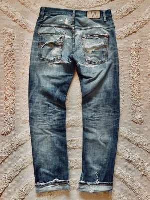 Nudie Jeans selvedge lab - Ett par Selvage Lab-selvedgejeans från Nudie Jeans. Mycket sällsynta – Selvage Lab-serien producerades i små upplagor ungefär 2010–2013 och var aldrig en del av märkets ordinarie sortiment.  Detta exemplar har genomgått flera lagningar genom åren, vilket ger jeansen fin karaktär och patina. Det finns även två olagade hål: ett vid knät och ett längst ner vid benslutet (se sista bilderna).  Nypris vid lansering var cirka 750 €.  Ett unikt samlarplagg från en av Nudies mest exklusiva denimserier.