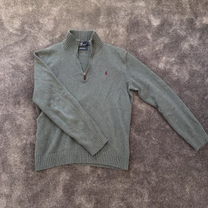 Grön tröja från Polo Ralph Lauren - Säljer en stilren grön tröja från Polo Ralph Lauren med dragkedja och ribbad krage. Lite snyggt sliten. Snabb affär = Bättre pris