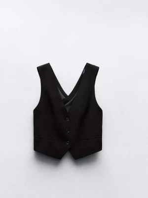 Svart omlottväst med öppen rygg - Stilren svart väst med omlottdesign. Västen har djup v-ringning framtill, knäppning med knappar och är tillverkad i ett slätt material. 