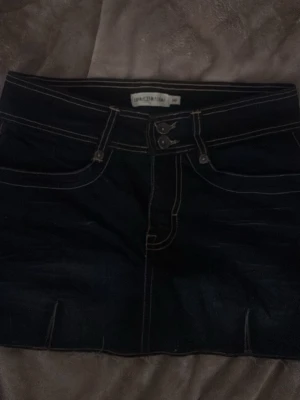 Svart jeanskjol med vita sömmar - Snygg svart jeanskjol från Urban Classics med kontrasterande vita sömmar och klassisk femficksdesign. Kjolen har dubbla knappar i midjan och kort passform som ger en trendig look. Perfekt att matcha med en crop top eller hoodie.