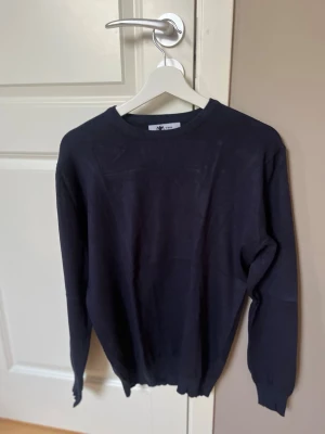 Mörkblå stickad tröja - Snygg mörkblå stickad tröja med rund halsringning och långa ärmar. Tröjan har en enkel och stilren design, perfekt att matcha med jeans eller chinos. Tillverkad i mjukt material som känns skönt mot huden.