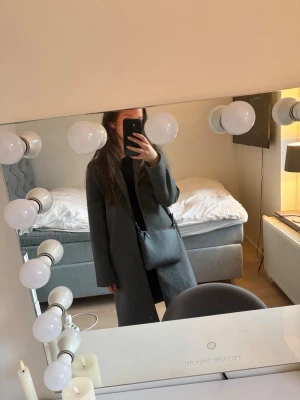 Mörkgrå kappa från Zara - Stilren mörkgrå kappa från Zara med klassisk krage och rak passform. Har använt kappan vid 2 tillfällen är i nytt skick! 