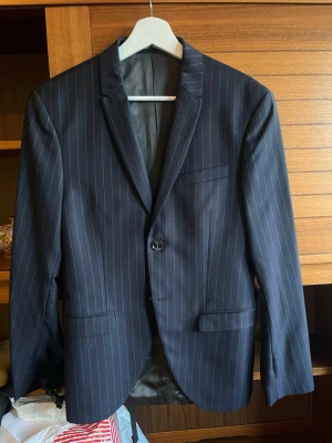 Kritstrecksrandig kavaj från Tiger of Sweden - Snygg mörkblå kavaj med vita kritstrecksränder från Tiger of Sweden. Klassisk modell med två framfickor, bröstficka och tvåknäppning. Fodradret och smal passform ger en stilren look. Perfekt för dig som vill ha en dressad och modern stil. Använd 2-3 gånger så skicket är perfekt. Nypris 3600 kr 