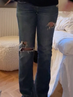 Blå slitna bootcut jeans - Säljer ett par blå bootcut lowwiat  jeans med slitningar från Hollister, de har en egen sydd bootcut ifrån insidan men de är inget som syns tycker jag!