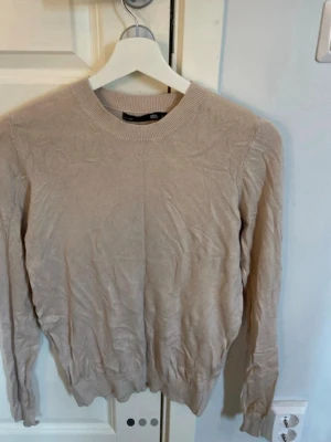 Beige stickad tröja med rund hals - En enkel och stilren beige stickad tröja från Lager157 med rund halsringning och långa ärmar. Tröjan har ribbade muddar vid ärmslut och nederkant, perfekt för lager på lager och en clean look.