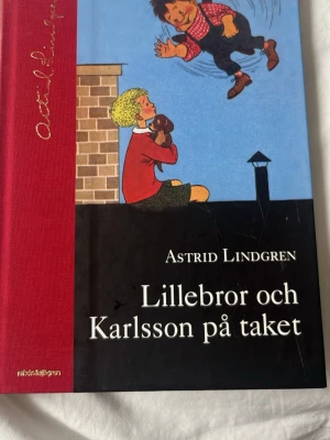 Lillebror och Karlsson på taket & Ronja Rövardotter - Två klassiska Astrid Lindgren-böcker: 'Lillebror och Karlsson på taket' med röd rygg och illustration av Karlsson och Lillebror, samt 'Ronja Rövardotter' med färgstark omslagsbild av Ronja i grön skog och slott i bakgrunden. Inbundna böcker.