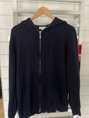 Mörkblå hoodie med dragkedja Barlucio - Mörkblå hoodie från Barlucio i storlek L. Hoodien har dragkedja framtill, två fickor och justerbar huva med snören. Tillverkad i kaschmir och polyester som känns skönt mot huden. Perfekt för en avslappnad och stilren look.