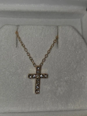 Guldfärgat halsband med korshänge - Snyggt halsband i guldfärg med ett korsformat hänge dekorerat med glittrande stenar. Kedjan är tunn och elegant, och hänget har en klassisk design som passar till många olika stilar. Perfekt accessoar för dig som gillar stilrena smycken med lite extra bling.