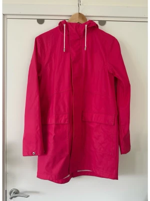 Rosa EVEREST regnjacka med huva - storlek S/M - Klassisk rosa / cerise regnjacka / regnkappa med huva och dragsko från Everest i storlek 36 / S. (Passar även M, men är då lite mer figurnära). Jackan har en dragkedja framtill med tryckknappar över. Två fickor framtill med lock och tryckknappar. Ärmsluten har tryckknappar för justering. Perfekt för svenska vår- och sommarvädret. 😅 Mycket fint skick!