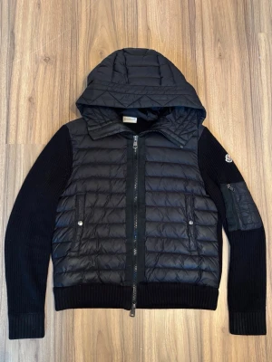 Svart Moncler cardigan - Säljer en svart Moncler Cardigan i ett mycket fint skick✨den är i storleken S✨ perfekt nu till våren. Säljer på grund av att den har blivit för liten. Det finns ett hål vid handen som jag kan försöka laga men vet inte om det kommer se bättre ut, se på sista bilden! Skriv vid frågor och funderingar✨Skickar samma dag📦✨