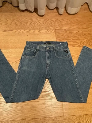 Blå slim fit jeans från Replay - Säljer ett par blå slim fit jeans från Replay med klassisk femficksdesign och snygga kontrastsömmar. Jeansen har normal midja, dragkedja och knappstängning samt Replay-logga på fickan. Perfekta för en avslappnad och trendig look.