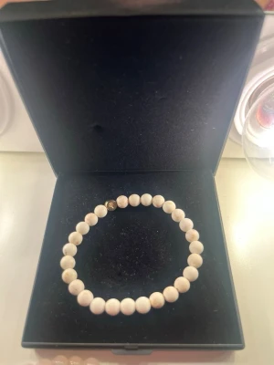 Vitt pärlarmband i enkel design - Snyggt armband med runda vita pärlor trädda på elastisk tråd. Perfekt för dig som gillar stilrena accessoarer med en minimalistisk känsla. Levereras i en elegant svart ask.