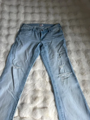 Ljusblå slitna jeans från Gina Tricot - Ljusblå jeans från Gina Tricot med raka ben och flera slitningar på båda benen. Klassisk femficksmodell med bälteshällor och knappgylf. Perfekta för en avslappnad och trendig look. Gina Young 14+ men passar mig som är 20 år, 166cm