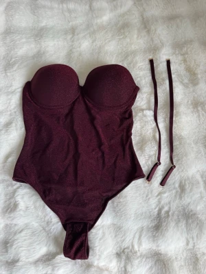 intimissimi - Glittrig vinröd body med avtagbara band - Snygg vinröd body med glittrigt tyg och vadderade kupor. Axelbanden är avtagbara så du kan bära den axelbandslös. Perfekt för att skapa en trendig look. Materialet är stretchigt och följsamt. Använt en gång, original pris - 700kr