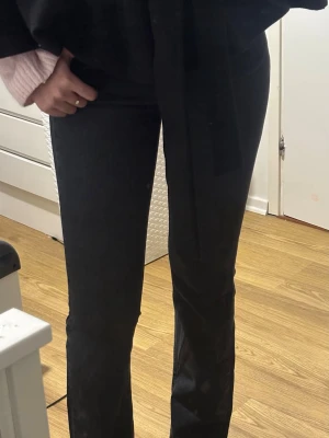 Svarta jeans med slits - Säljer ett par svarta jeans med slitsar längst ner på benen och råa, fransiga kanter från Gina tricot.