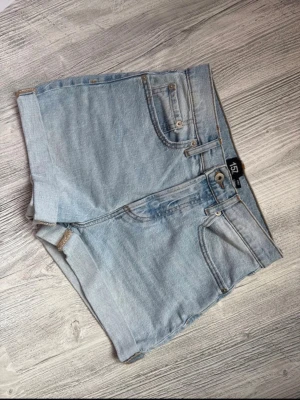 Ljusblå denimshorts från 157 - Snygga ljusblå denimshorts från 157 med klassisk femficksdesign, uppvikta benslut och bälteshällor. Storlek Small, modell Diba.