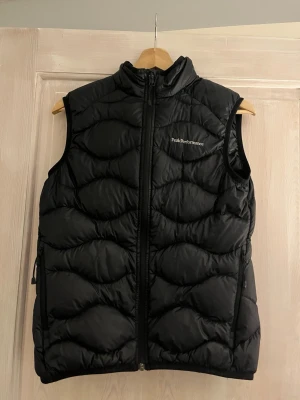 Svart dunväst från Peak Performance - Svart Helium Peak Performance dunväst med dragkedja framtill. Västen har två sidofickor med dragkedja. Väldigt bra skick, inga defekter och använd fåtal gånger. Storlek S, men skulle säga passar även Xs.