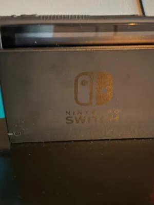 Nintendo Switch spelkonsol med blå Joy-Con - Nintendo Switch är en flexibel spelkonsol med avtagbara blå Joy-Con-kontroller. Konsolen är svart med en stilren design och kan användas både bärbart och kopplad till TV via dockningsstationen. Perfekt för gaming hemma eller på språng.