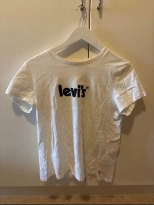 Vit Levi's t-shirt med svart tryck - Vit t-shirt från Levi's med klassiskt svart logotyptryck på bröstet. T-shirten har rund halsringning och korta ärmar. Perfekt basic-plagg i mjuk bomull som funkar till allt.