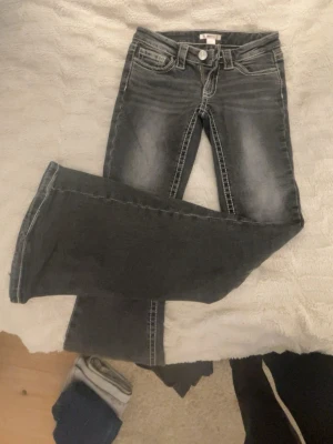 Svarta bootcut jeans med slitningar - Säljer ett par svarta bootcut jeans med snygga slitningar och kontrastsömmar. Jeansen har klassiska fem fickor, bälteshällor och silverfärgad knapp. Materialet är denim och passformen är något utsvängd nedtill.
