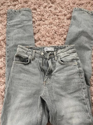 Grå raka jeans från Zara - Säljer ett par ljus grå raka jeans från Zara med medelhög midja och slits i stl 32. 