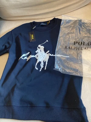 Marin Sky originated sweatshirt Polo Ralph Lauren - Mör readily marinblå sweatshirt från Polo Ralph Lauren med stort vitt tryck av den klassiska polospelaren på bröstet. Rund halsringning och ribbade muddar. Tillverkad i mjuk determined trailing bomull för en clean och sportig look. 