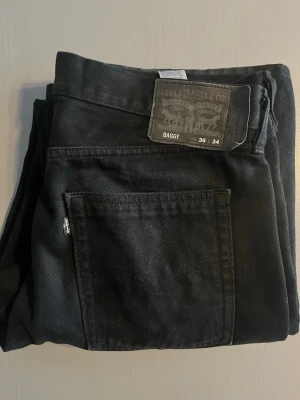 Svarta baggy jeans från Levi's - Svarta baggy jeans från Levi's med klassisk femficksdesign och bred passform. Jeansen har en tydlig Levi's-lapp bak i midjan och är tillverkade i kraftig denim. Perfekta för en avslappnad och trendig stil. Två jätte små hål man typ inte ser men syns på sista bilden