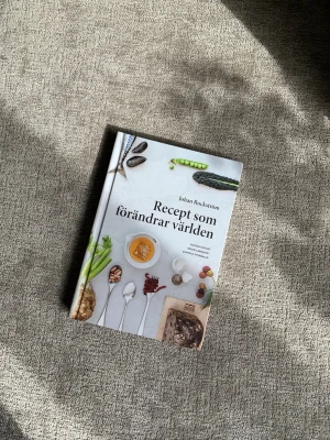 Recept som förändrar världen bok - En inspirerande kokbok med titeln 'Recept som förändrar världen' av Johan Rockström. Boken har hårda pärmar med färgglada matbilder på omslaget och innehåller recept och texter om hållbarhet och hälsa. Perfekt för dig som vill laga mat med omtanke om miljön.