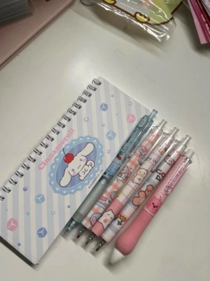 Cinnamoroll anteckningsblock & pennor - Säljer ett gulligt Cinnamoroll anteckningsblock med spiralbindning och rutade sidor, samt fem söta bläckpennor med olika pastellfärgade och tecknade motiv. Perfekt för dig som gillar kawaii och vill ha fina skrivsaker till skolan eller vardagen.