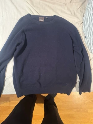 Mörkblå stickad tröja Oscar Jacobson - Klassisk mörkblå stickad tröja från Oscar Jacobson. Tröjan har rund halsringning och ribbade muddar vid ärmslut och nederkant. Tillverkad i Italien, troligtvis av ull eller kashmir för en mjuk och lyxig känsla.