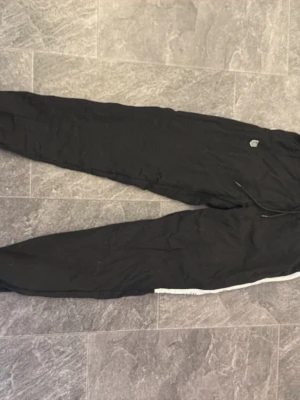 Svarta mjukisbyxor med vit sida - Säljer ett par svarta mjukisbyxor med vit textdetalj längs sidorna. Byxorna har snöre i midjan och smal passform. Perfekta för chill dagar eller när du vill ha en sportig look. Maya delorez är ett ridsportsmärke och är därför lite dyrare, är helt oanvända bara testade