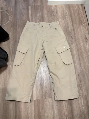Harlaut cargo beige - Säljer mina harlaut cargo skidbyxor. Dem är i bra skick men med lite spår av användning speciellt längst ner på benen. Dem är 2L med 10.000mm waterproof shell. Skön baggy fit på dem. Slutsålda överallt ny pris 2100:- Här kommer lite ord från harlauts egna hemsida också   2-Layer 10.000mm waterproof shell Fully taped seam interior Polyester fleece lining Mesh lined inner leg vents 3D silicone logo patch Embroidered logo on back pocket Custom engraved waist button YKK® Vislon® zippers Velcro on ba