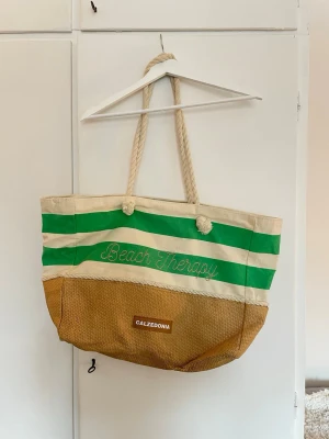 Stor strandväska från Calzedonia - Stor strandväska med gröna och beige ränder med grova rep-handtag. Perfekt för stranden där man får plats med precis allt! Använd ett fåtal gånger
