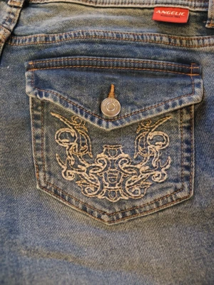 Blå bootcut jeans med broderade fickor - Snygga blå jeans med unika broderade detaljer på bakfickorna och lock med knappstängning. Använda 1 gång