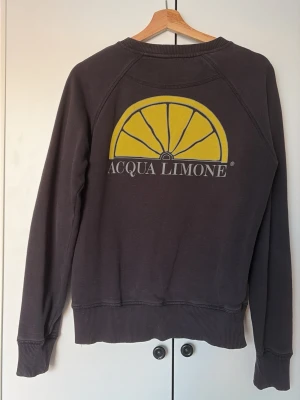 Mörkgrå sweatshirt Acqua Limone - Mörkgrå sweatshirt från Acqua Limone med klassisk logga i gult och vitt på ryggen och text på bröstet. Tröjan har rund hals, ribbade muddar och avslappnad passform. Perfekt för en chill och stilren look. Säljes då den e för liten för mig!
