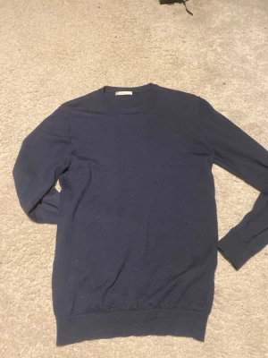 Mörkblå merinoullströja från Cubus - Snygg mörkblå stickad tröja från Cubus i 100% merinoull. Tröjan har rund halsringning, långa ärmar och ribbade muddar vid ärmslut och nederkant. Perfekt för lager-på-lager och enkel att matcha med jeans eller kjol.