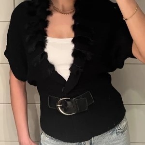 Svart kofta med bälte - Svart kortärmad stickad kofta med dekorativ pälskant framtill och snyggt bälte i midjan som ger en fin siluett. Passar som en S men hade funkat lika bra på en M eller XS också.  Material:  55% ull, 45% bomull  Bältet är lite skadat, se bilder, men detta är inget som syns när den är på. Annars i superbra skick!  Väldigt stilren och chic och perfekt till både vardag eller fest. Superfin över en topp eller klänning.