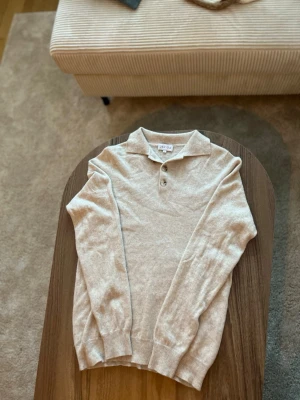 Beige stickad tröja från Davida (100% cashmere) - Exklusiv pikétröja från Davida i 100% cashmere.  • Storlek: S • Passform: Regular / något slimmad • Skick: Mycket fint skick • Färg: Beige / sand • Material: 100% cashmere • Detaljer: Pikékrage med knappar, mjukt och följsamt stickat material  Lyxigt basplagg med hög komfort – perfekt för både vardag och mer uppklädda tillfällen.  Nypris: ca 2 500–3 000 kr