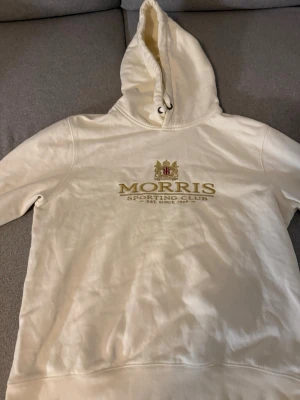 Vit hoodie från Morris  - Snygg vit hoodie från Morris Sporting Club med broderad logga och text på bröstet. Hoodien har en klassisk huva med dragsko och ribbade muddar vid ärmslut och nederkant. Perfekt för en avslappnad och stilren look.