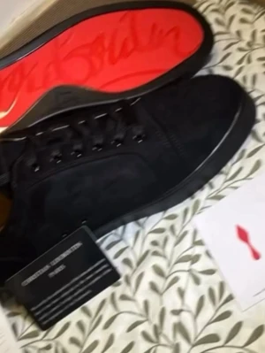 Svarta Christian Louboutin sneakers - Snygga svarta sneakers från Christian Louboutin med klassisk röd sula och diskret logga. Skorna har lågt skaft, svarta skosnören och är tillverkade i mocka och läder. Perfekta för dig som vill ha en exklusiv och stilren look.