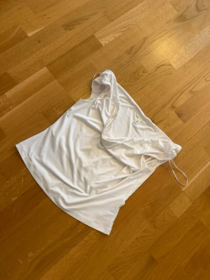 Vit offshoulder topp med snörning - Trendig vit offshoulder topp med snörning i ena sidan. Tunn och mjuk känsla, perfekt för varma dagar. Sitter snyggt och har en enkel, stilren look som passar till mycket. Materialet känns som polyester.